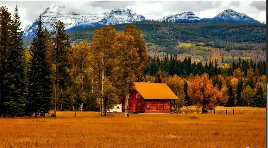 Rural cabin tucked against snow-capped mountains in fall
